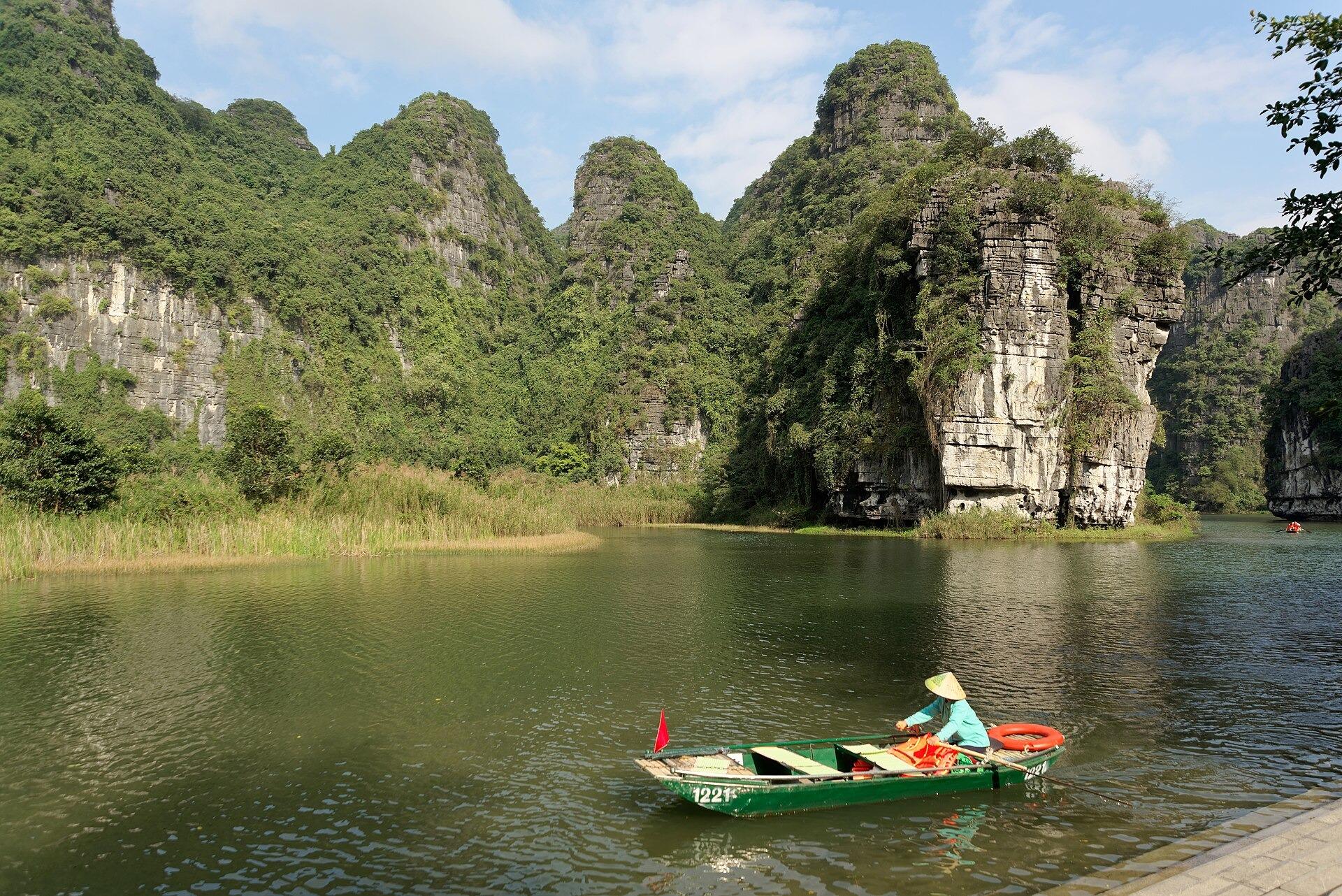 A woman rowing a small boat on the river below limestone cliffs at Tràng An, Ninh Bình